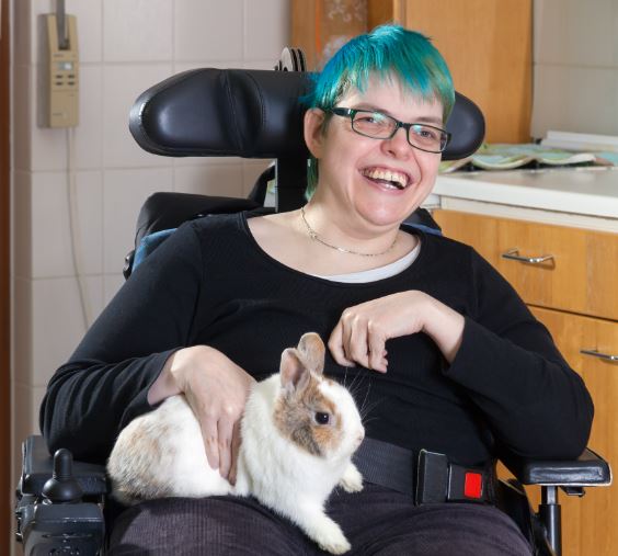 A woman sits in a wheelchair while smiling and holding a pet rabbit