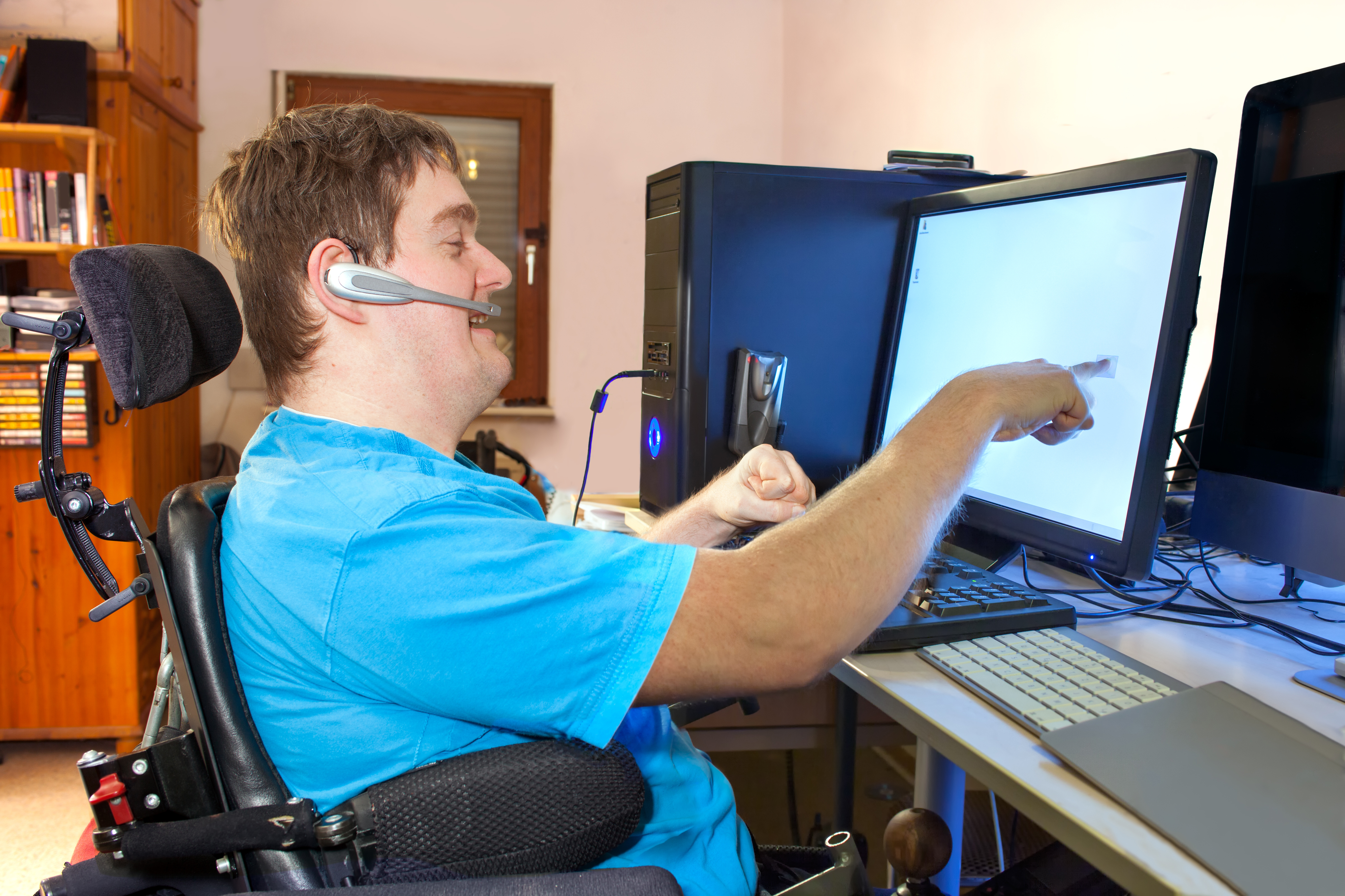 Man in wheelchair using a computer with an assistive touch screen and a headset microphone